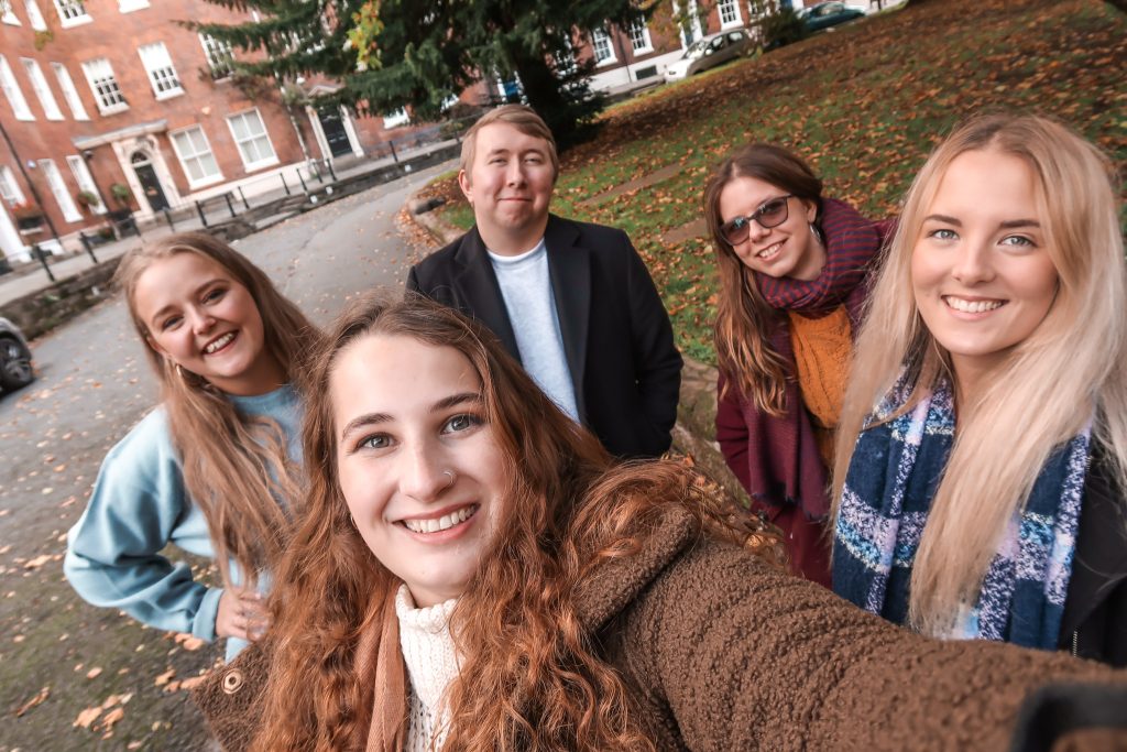 Casey is in the front of the shot taking a selfie with her fellow University Insiders behind her. Left to right we have Olivia, Kieran, Charlie and Sophie. Everyone is looking happy amongst the autumn leaves. 